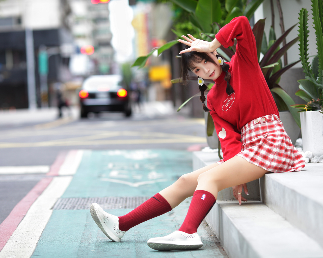 Веселая девушка азиатка в красном костюме сидит на ступеньках 