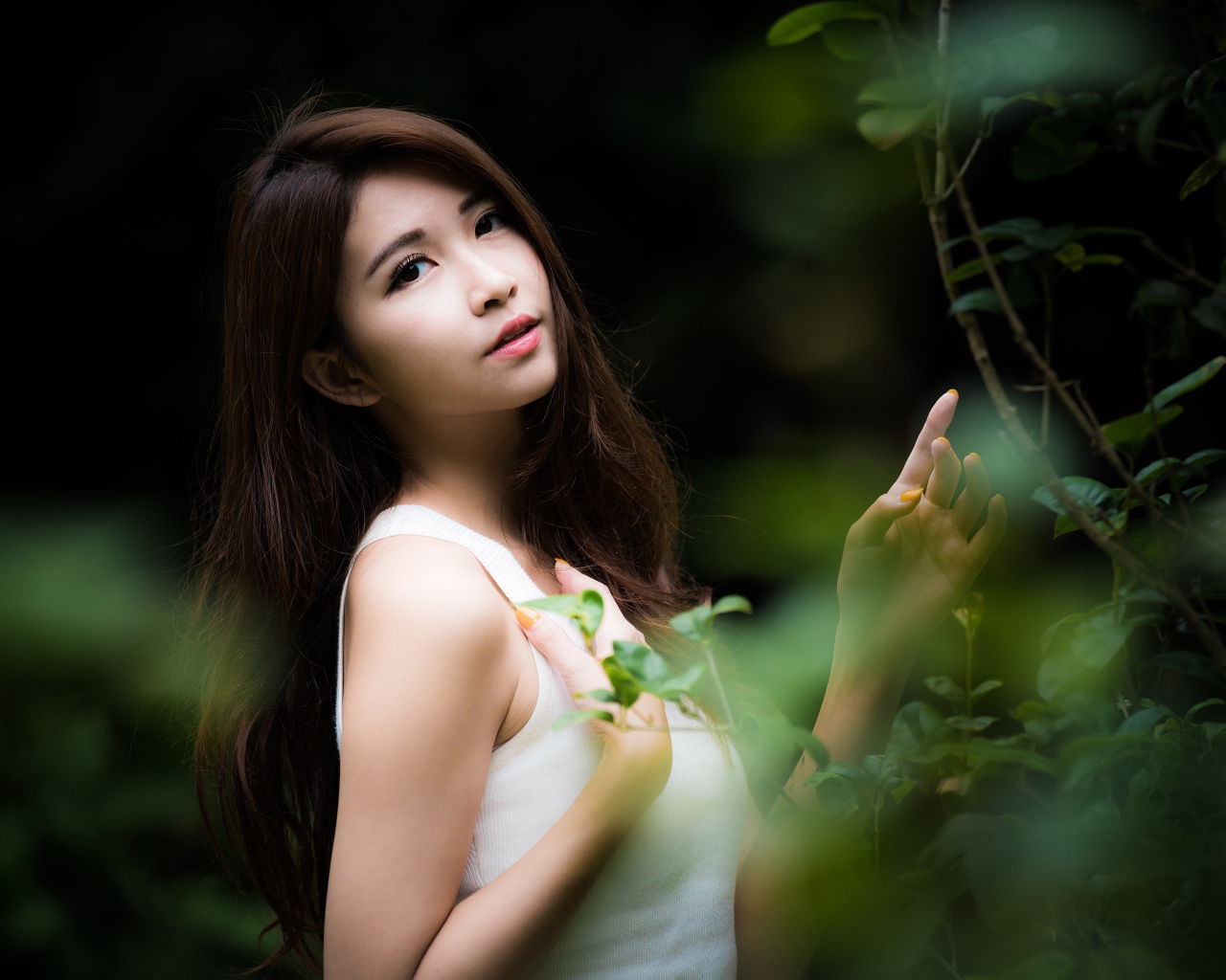 Милая азиатка в белом стоит у зеленых листьев