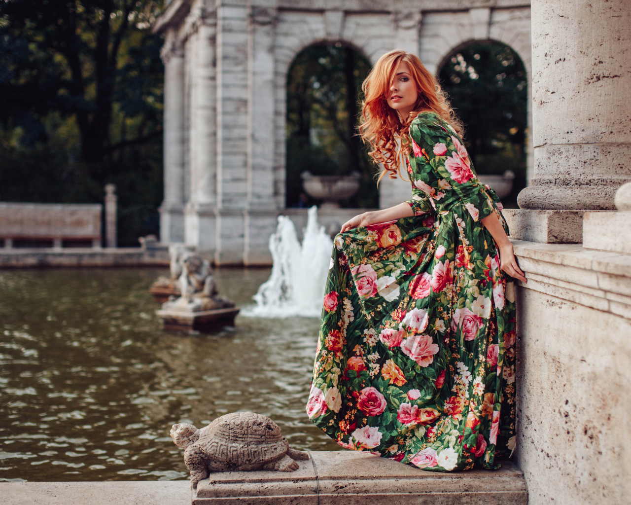 Девушка в красивом цветастом платье у пруда в парке 