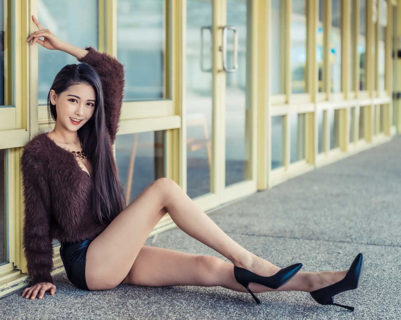 Девушка в свитере сидит у стеклянной стены 