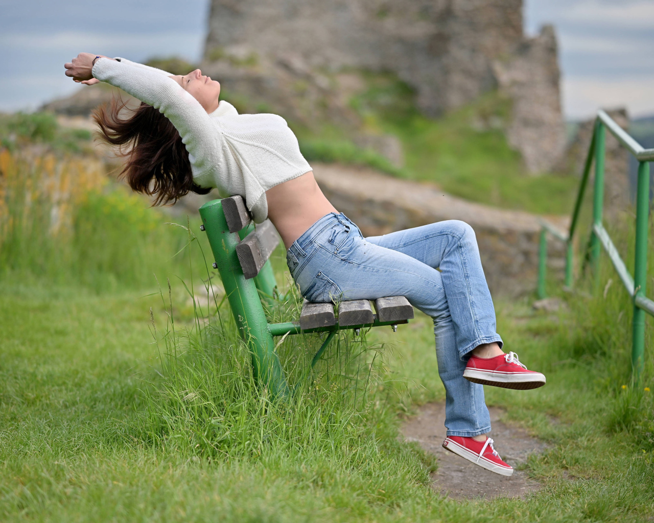 Девушка в синих джинсах сидит на лавке 