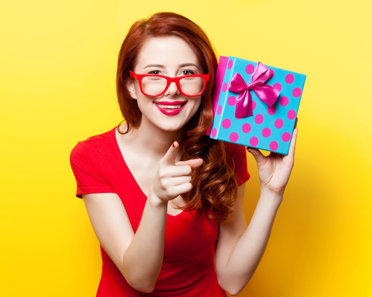Девушка в очках с подарком в руке на желтом фоне