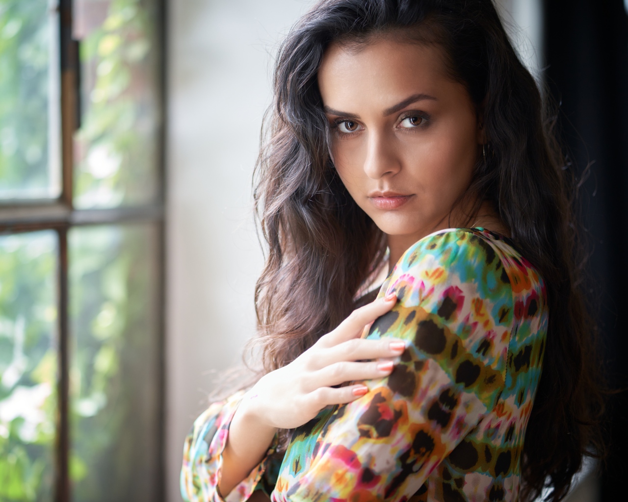 Длинноволосая кареглазая девушка стоит у окна
