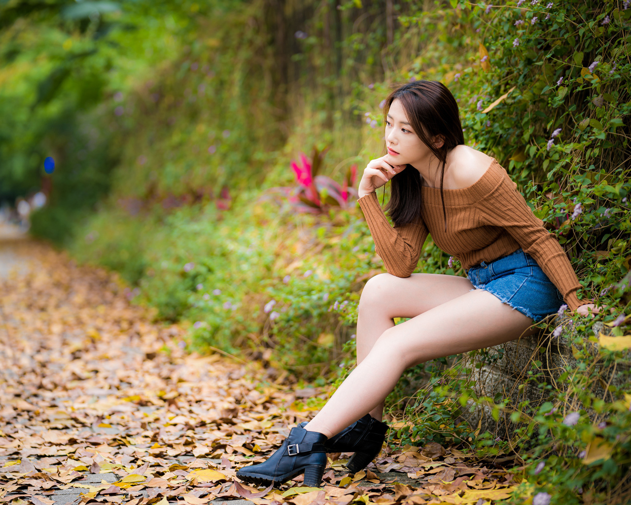 Задумчивая азиатка сидит в парке осенью 