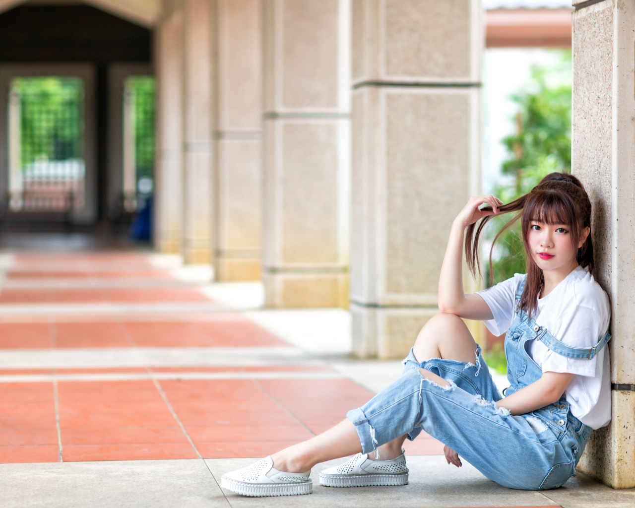 Грустная девушка азиатка сидит у колонны