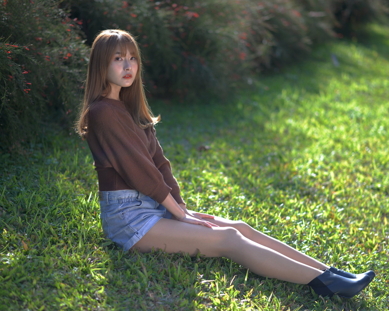 Грустная девушка азиатка сидит на зеленой траве 