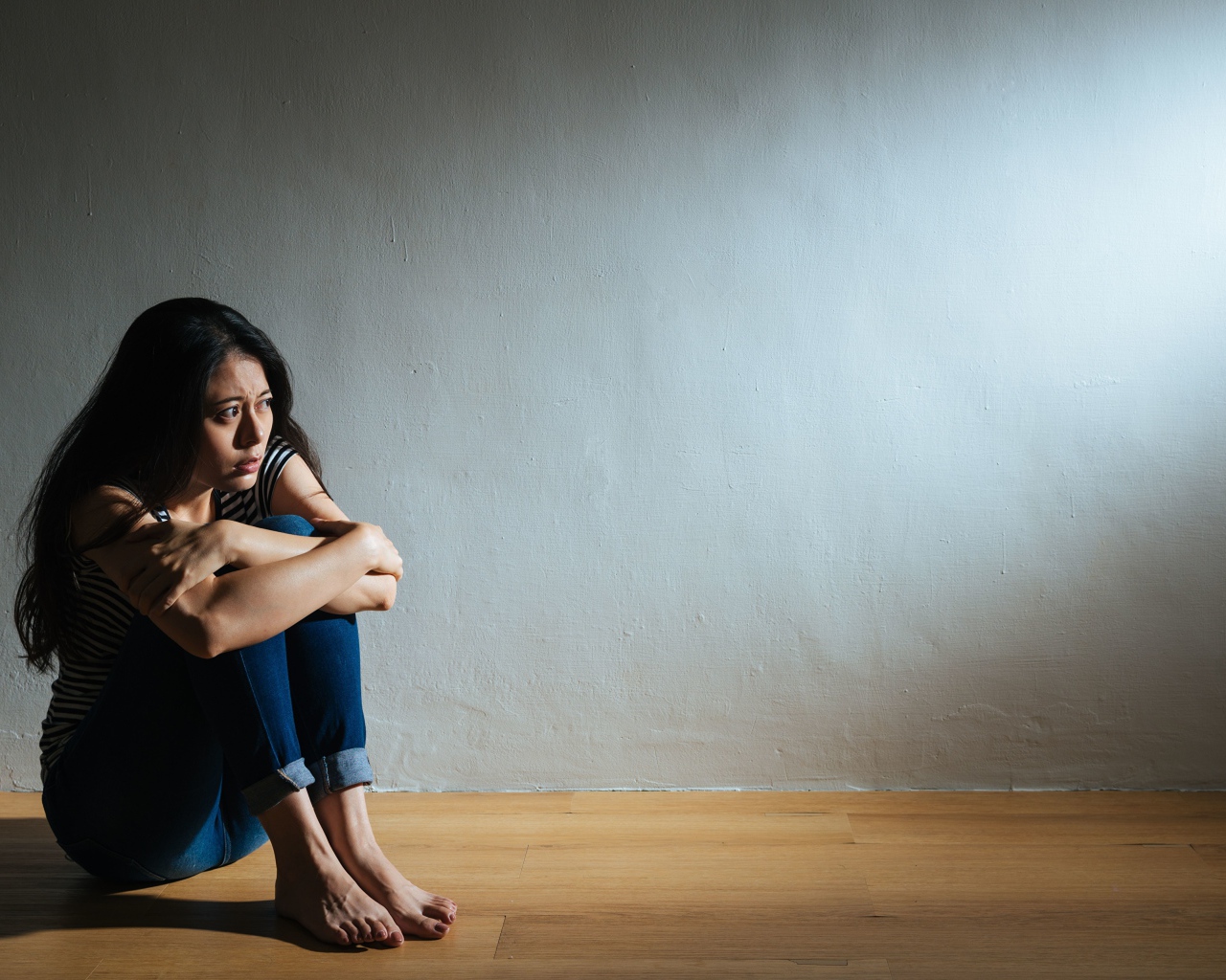 Испуганная девушка азиатка сидит у стены