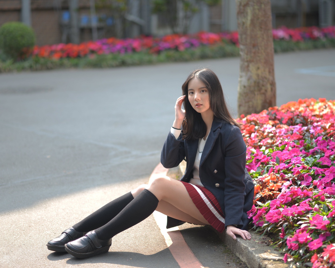 Девушка школьница сидит на земле у клумбы 