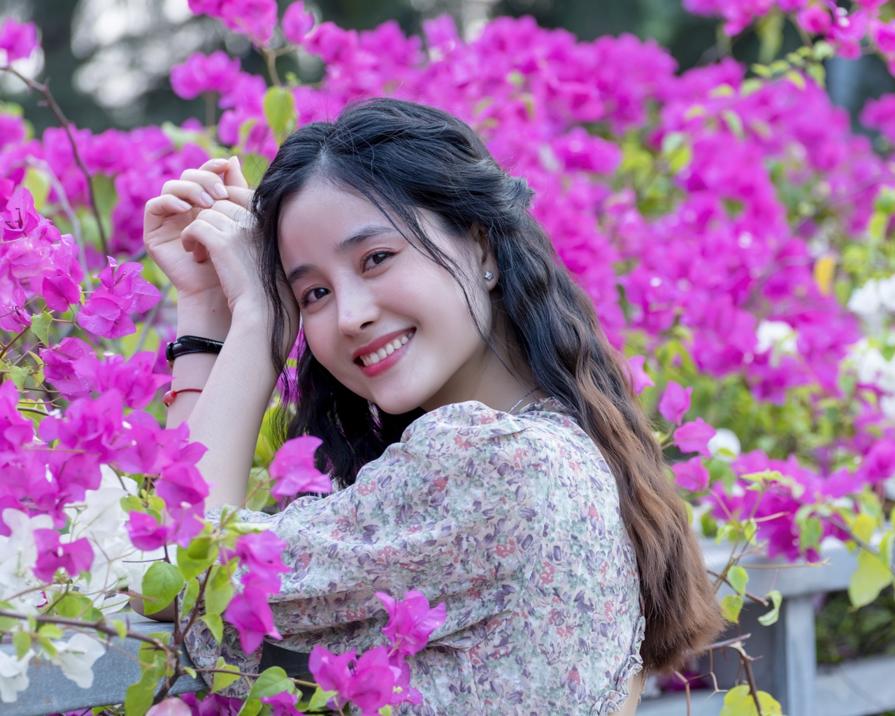 Улыбающаяся девушка азиатка на фоне розовых цветов