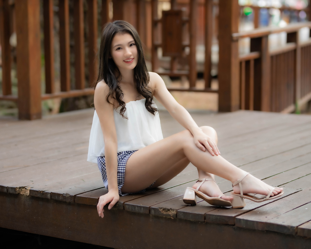 Улыбающаяся девушка азиатка сидит на мосту 