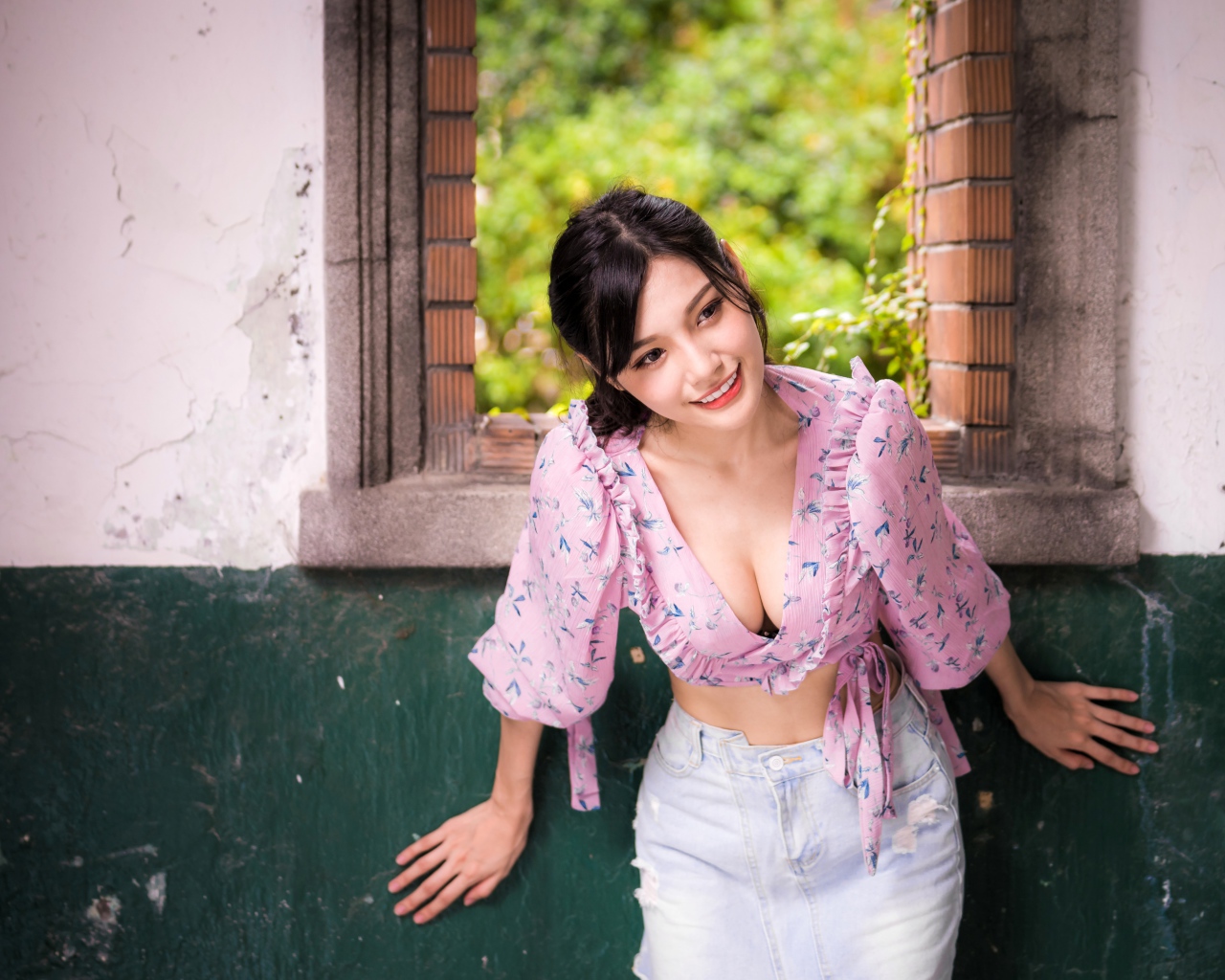 Улыбающаяся девушка азиатка стоит у окна 