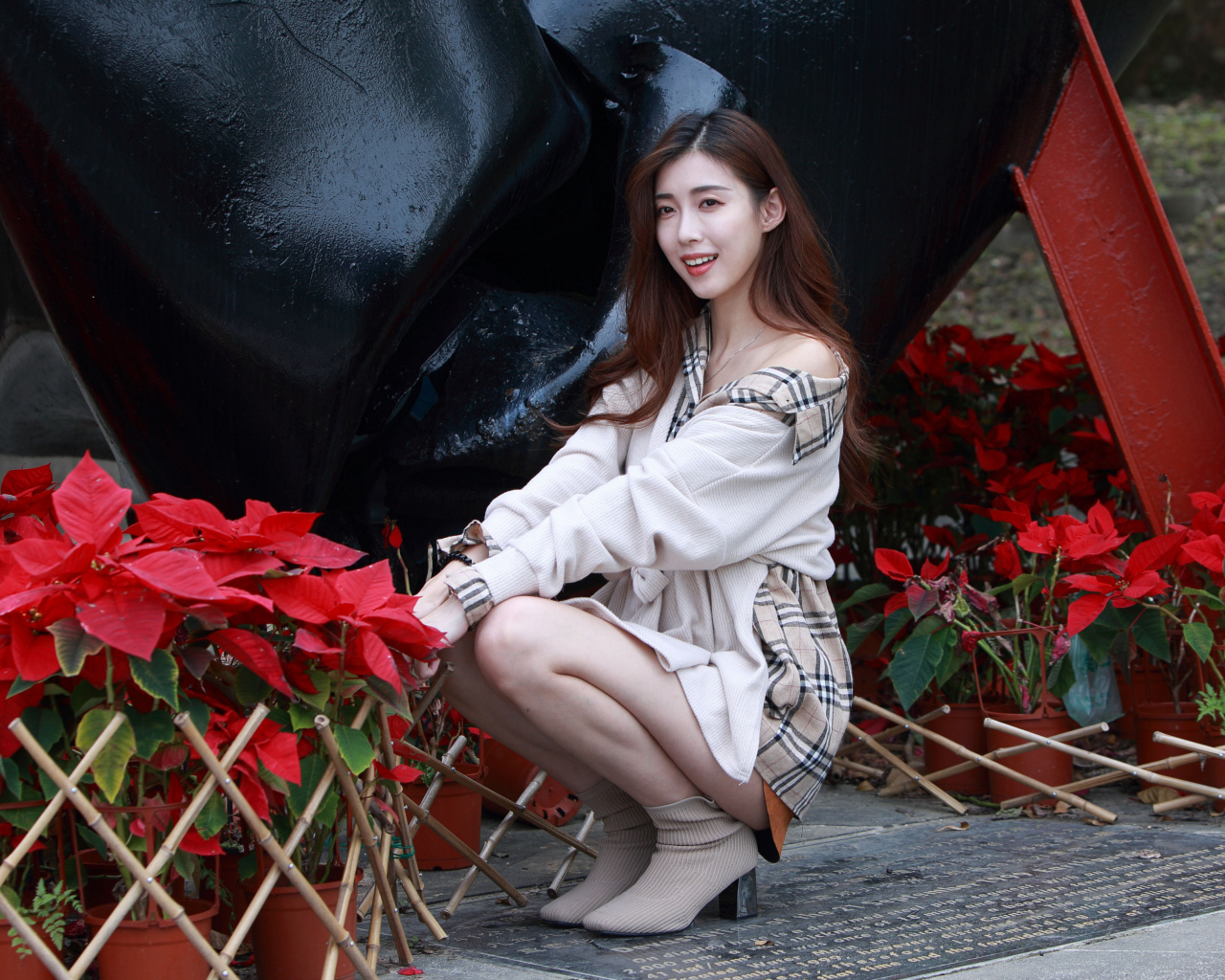 Улыбающаяся азиатка сидит у красных цветов 