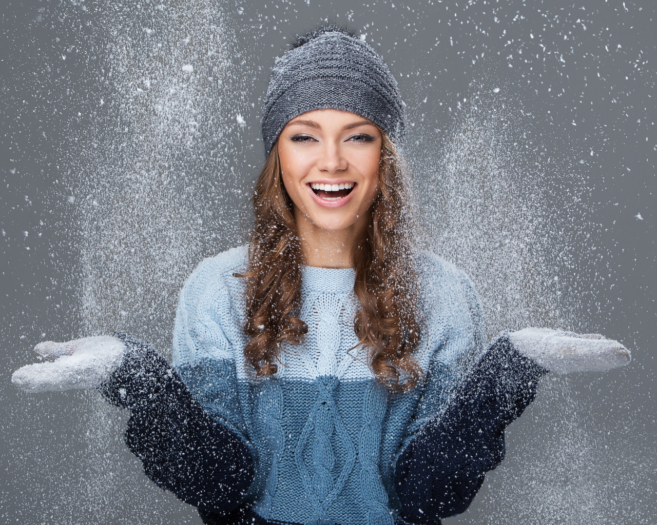 Улыбающаяся девушка ловит снег руками на сером фоне