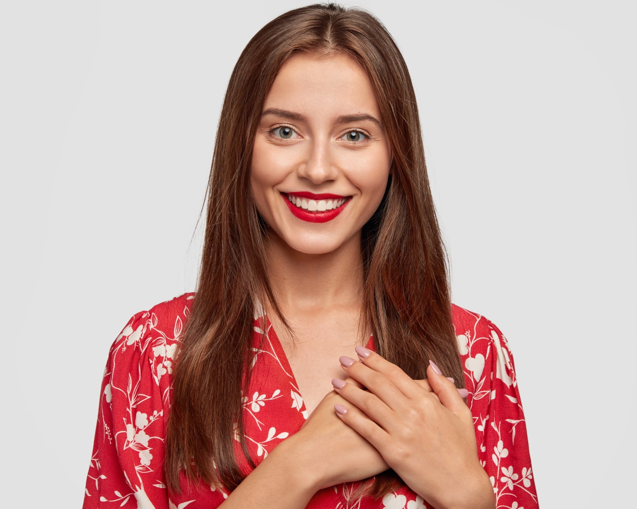 Улыбающаяся девушка с руками на сердце на сером фоне