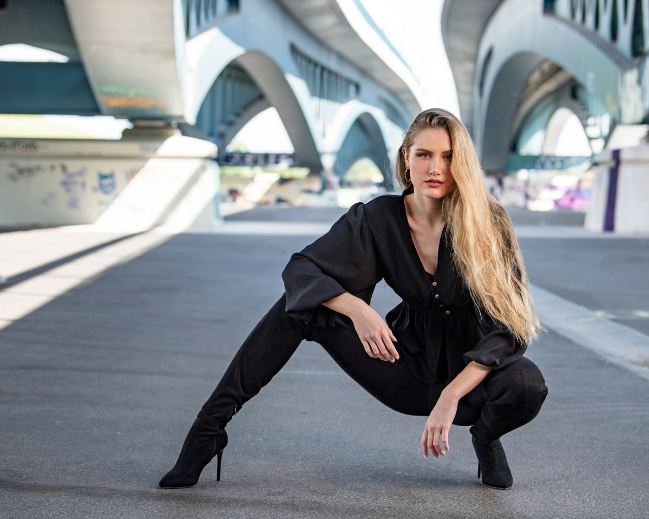 Стильная девушка в черном костюме под мостом