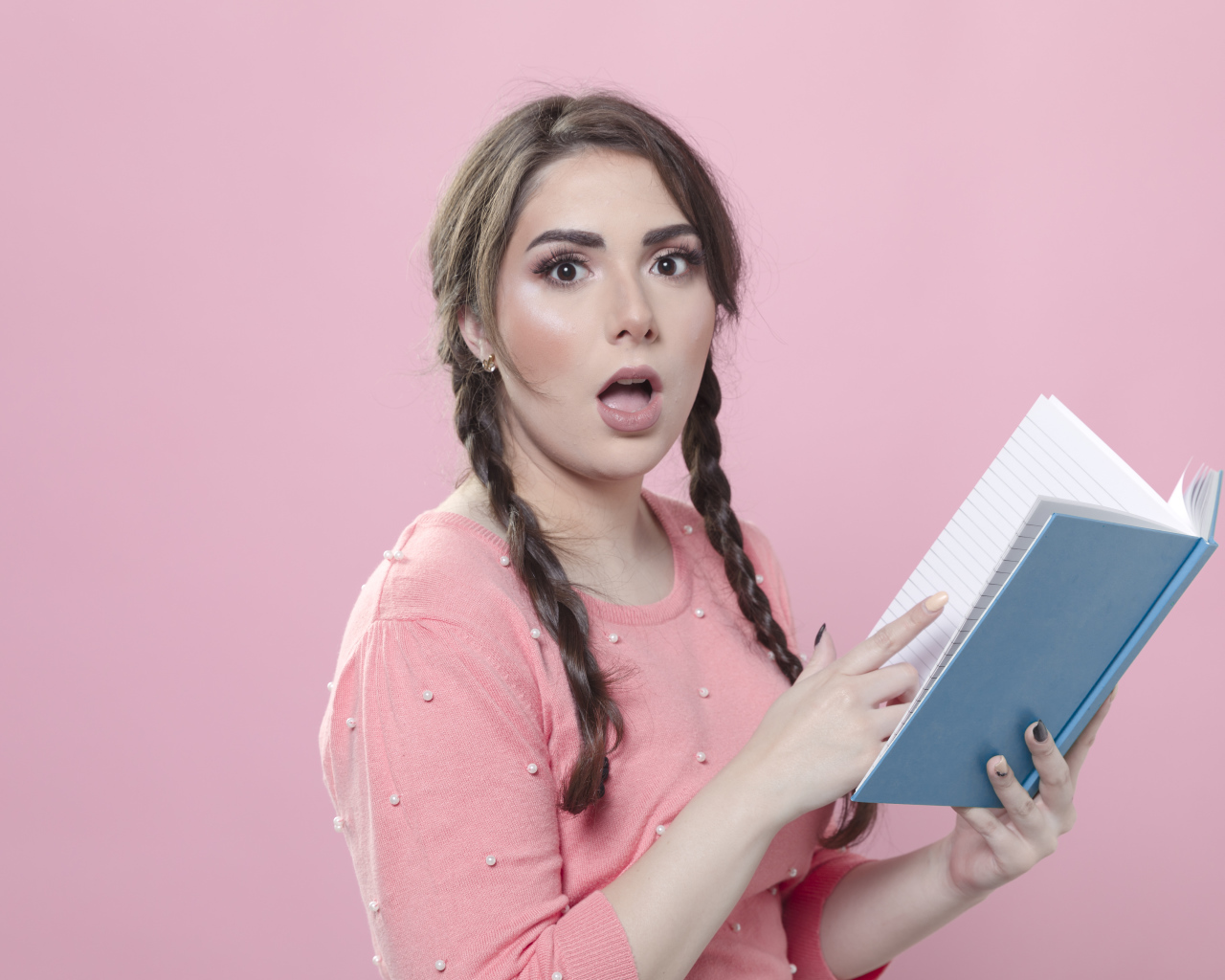 Удивленная девушка с книгой на розовом фоне
