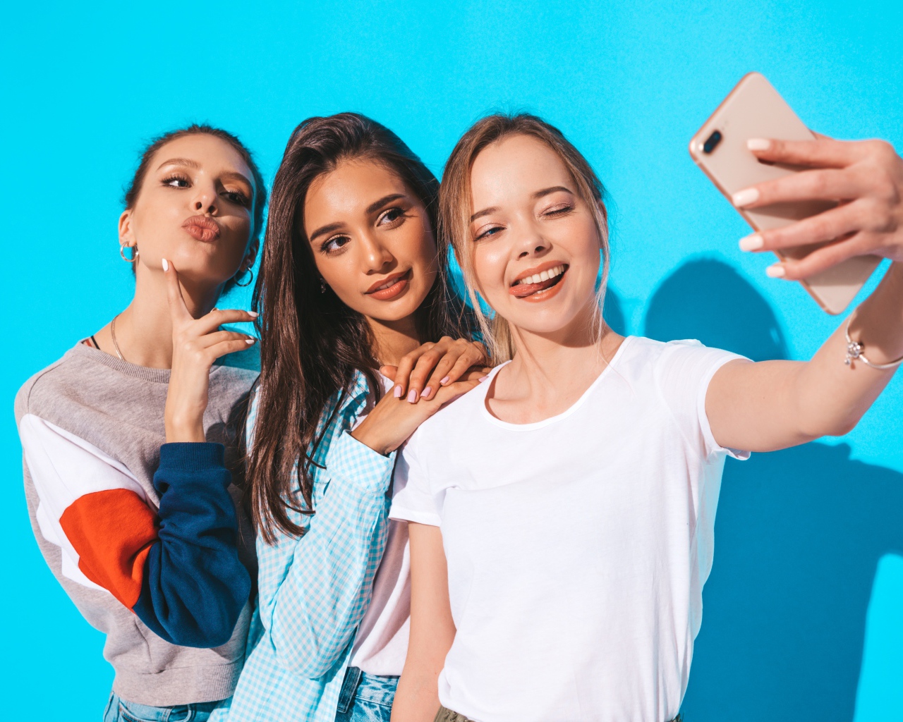 Три подруги делают селфи на голубом фоне