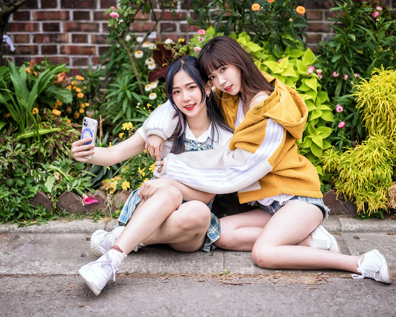 Две девушки азиатки сидят у стены с цветами 