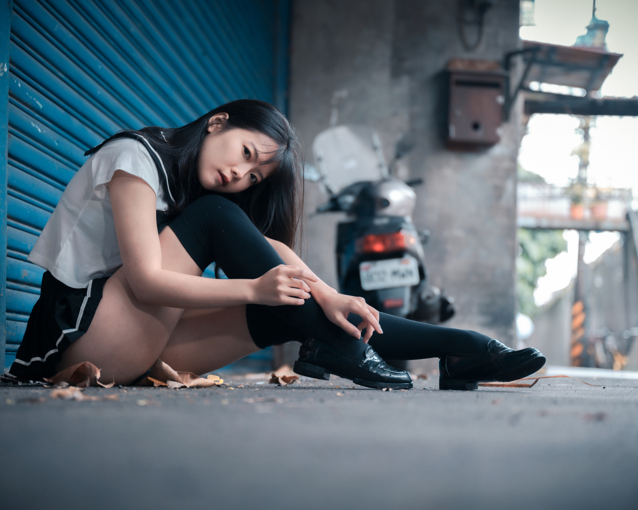 Молодая азиатка в черных чулках сидит у стены 