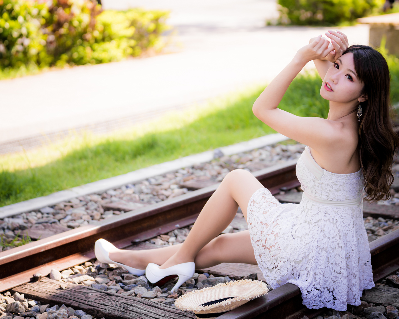 Молодая азиатка в белом платье сидит на рельсах 