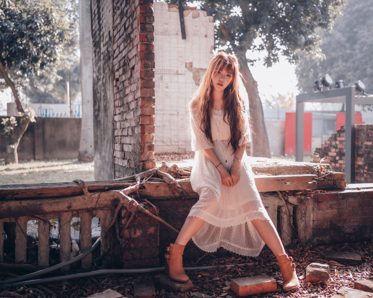 Молодая девушка азиатка в белом платье сидит на разваленной стене