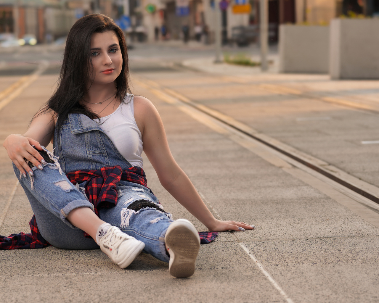 Молодая девушка в джинсовом наряде сидит на асфальте