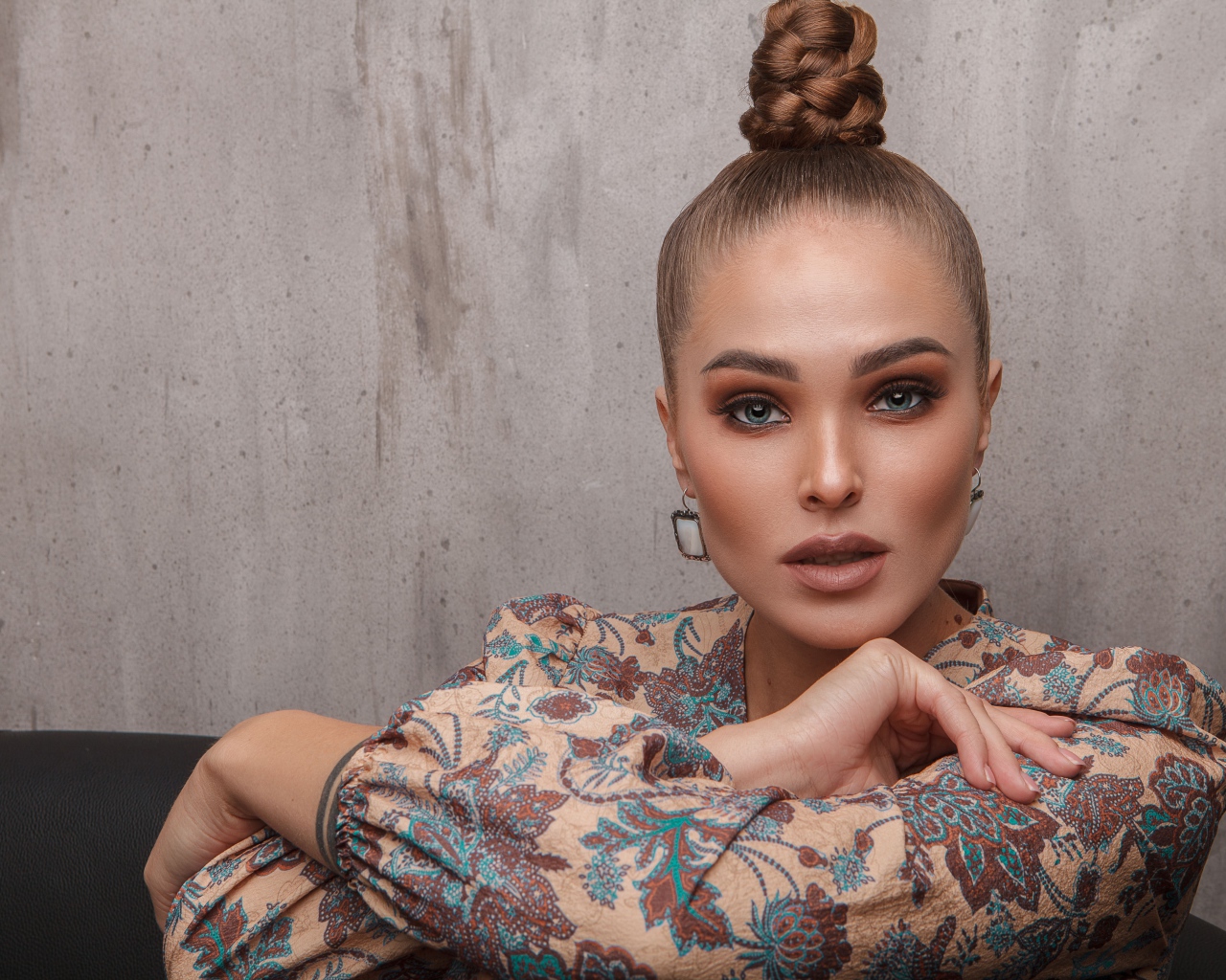 Молодая девушка с прической на голове на фоне стены