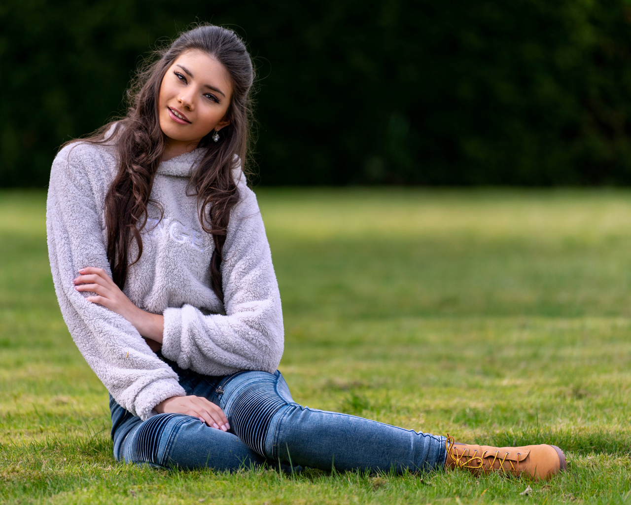 Молодая длинноволосая девушка сидит на траве 