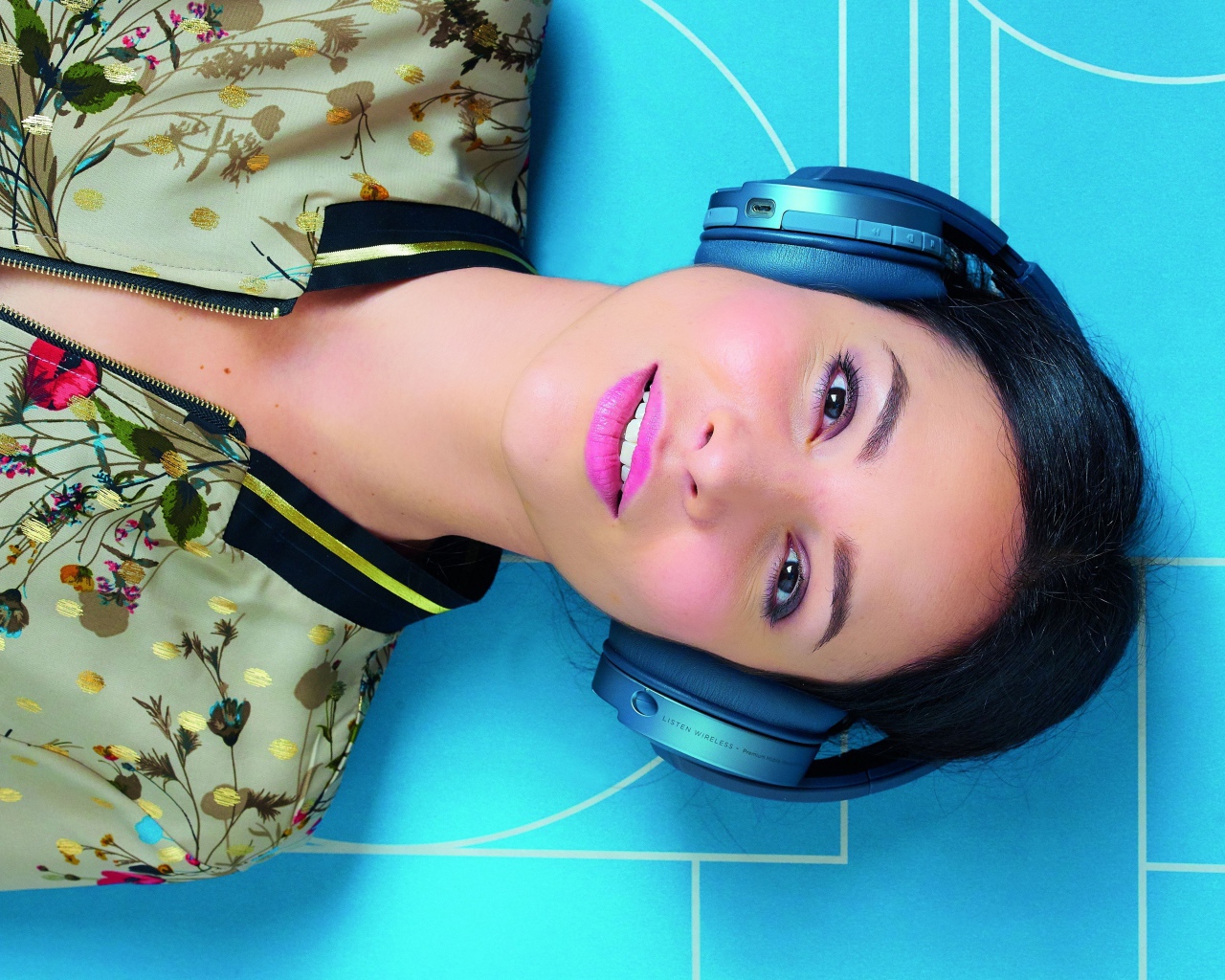 Молодая женщина в наушниках лежит на голубом полу