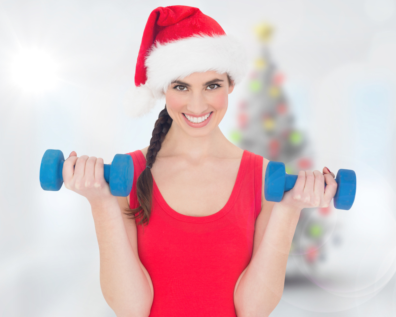 Красивая девушка в шапке Санта Клауса с гантелями в руках 