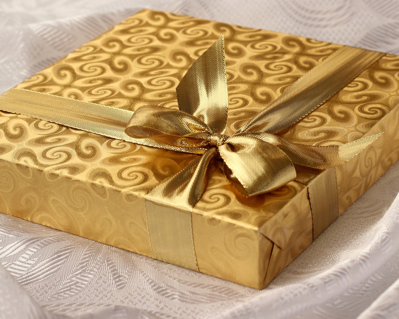 Красивая золотистая коробка с подарком на кровати 