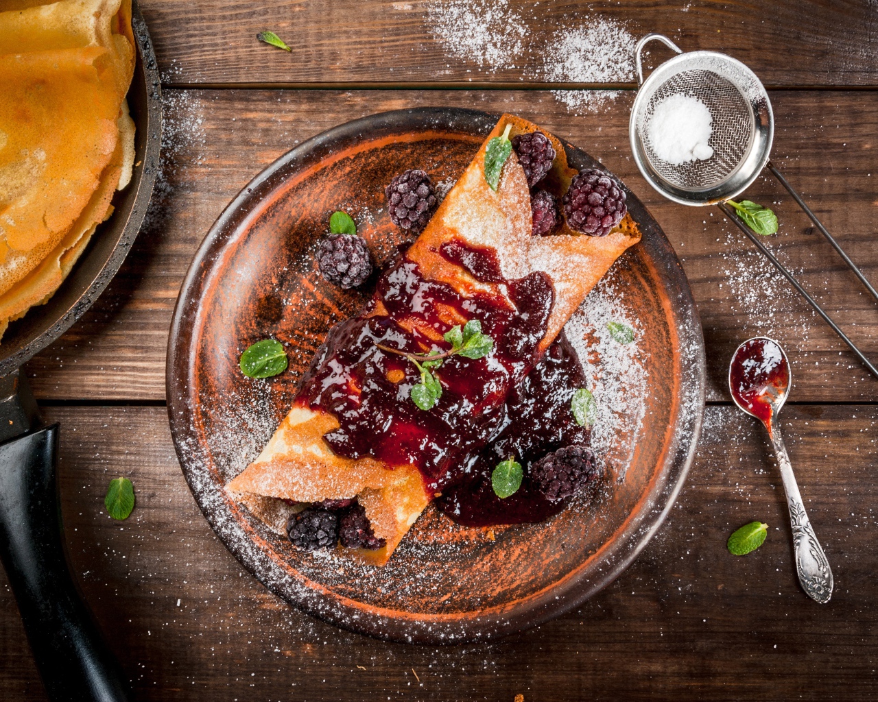Блин с ягодами и джемом на тарелке с сахарной пудрой
