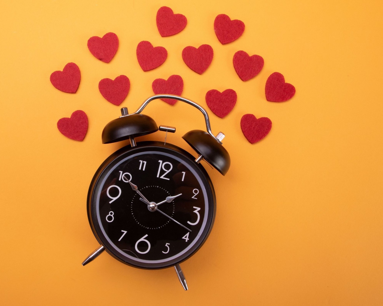 Черный будильник с сердечками на оранжевом фоне