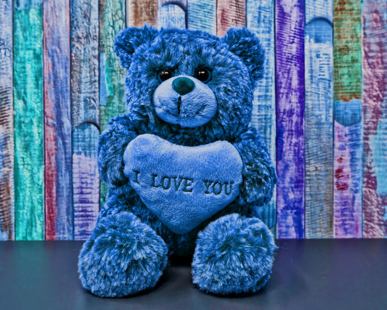 Синий медведь с сердцем на фоне забора