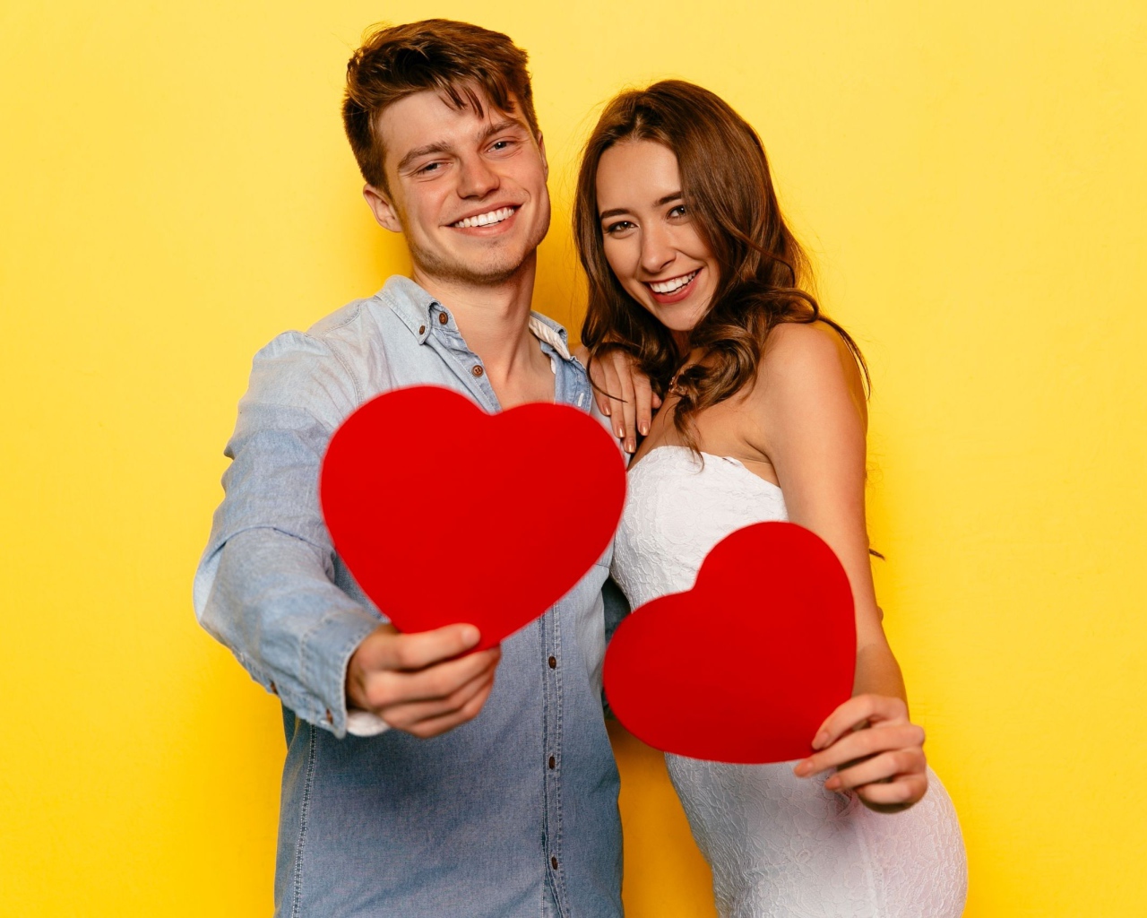 Влюбленная пара на желтом фоне с бумажными сердечками в руках 