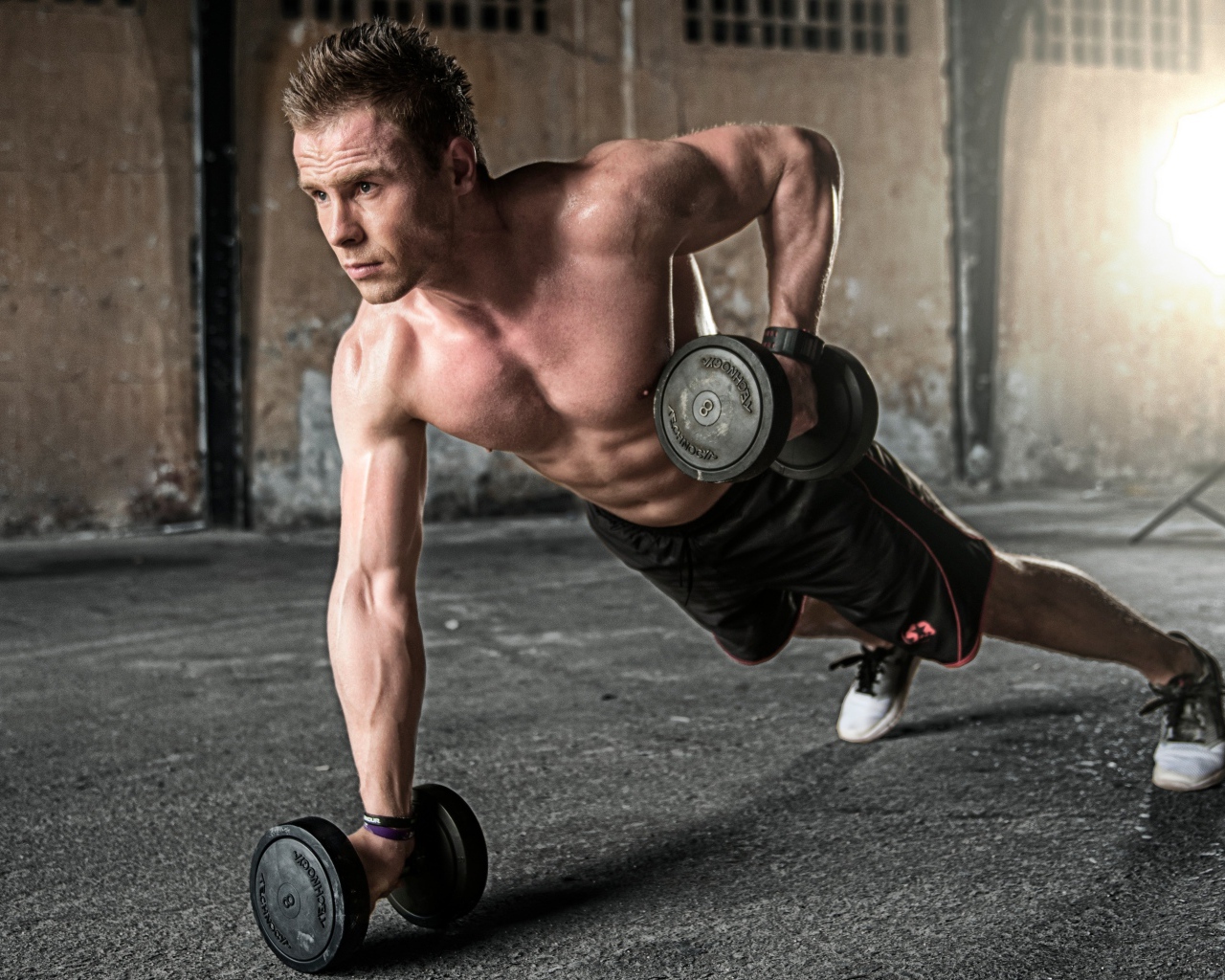 Спортивный мужчина качает руки гантелями