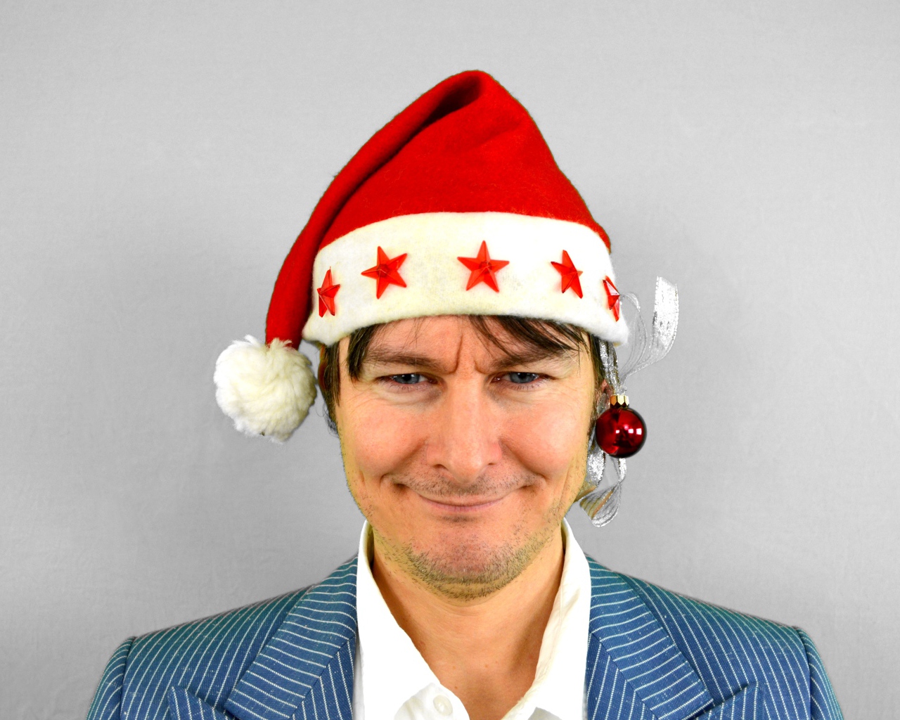 Голубоглазый мужчина в новогодней шапке на сером фоне 