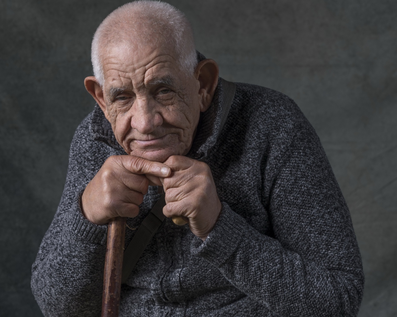 Пожилой мужчина в теплом свитере на сером фоне 