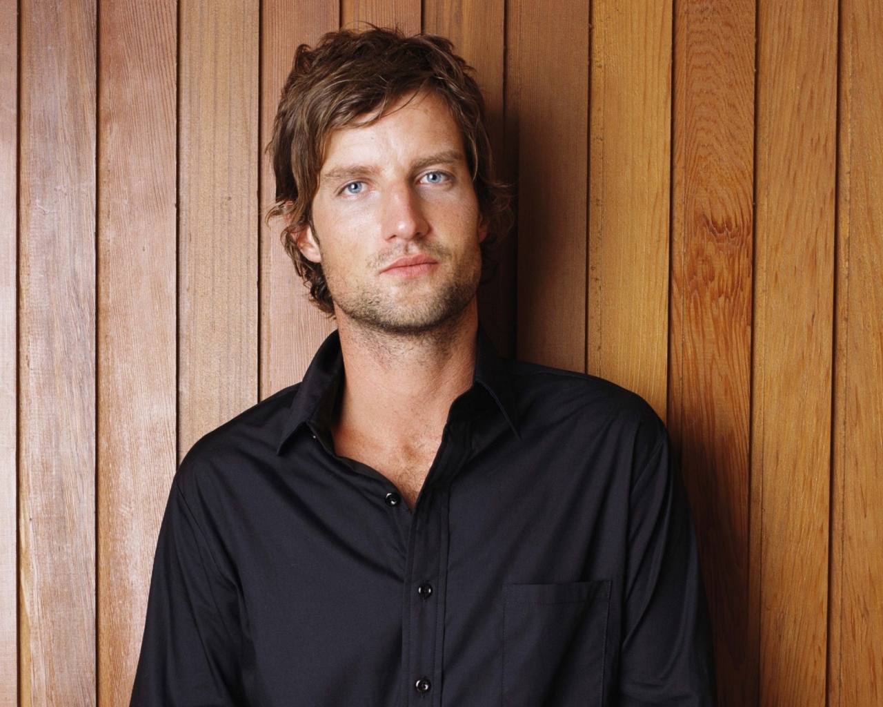 Красивый мужчина в черной рубашке на деревянном фоне