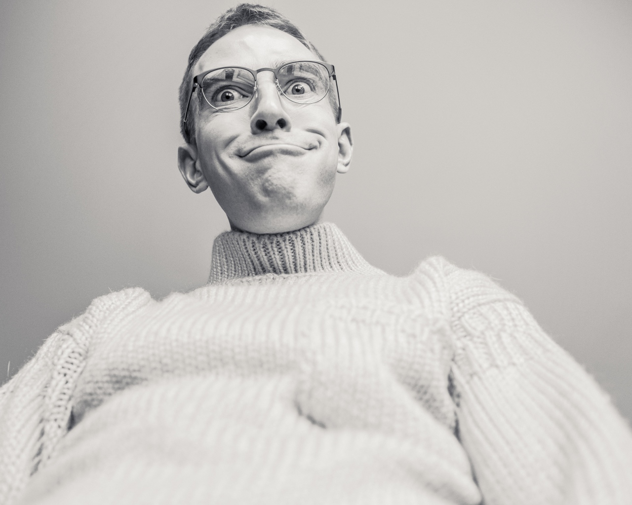 Мужчина в очках корчит лицо на сером фоне