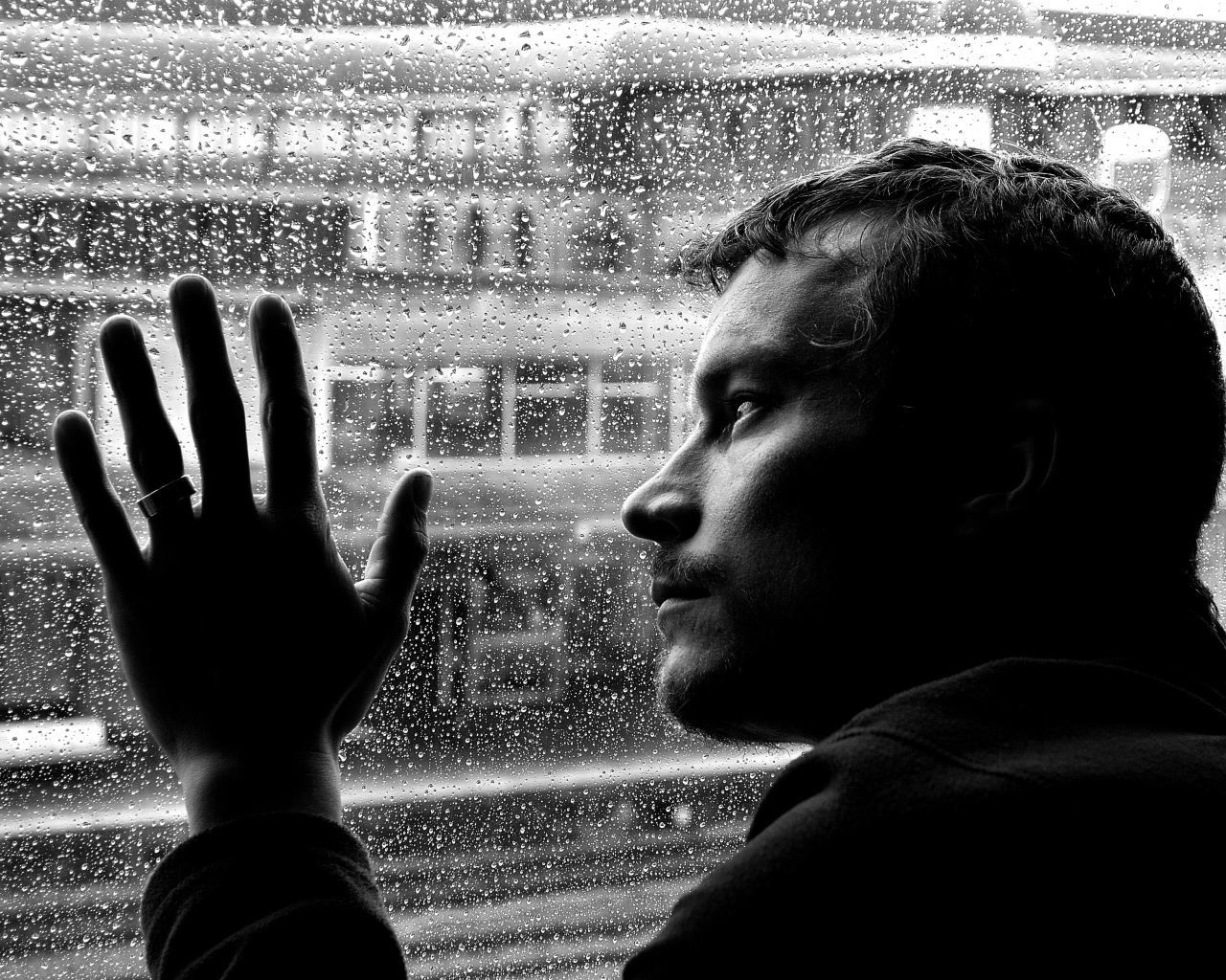 Грустный мужчина стоит у мокрого окна 