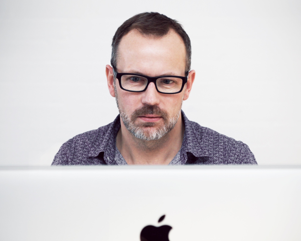 Серьезный мужчина в очках сидит за макбуком