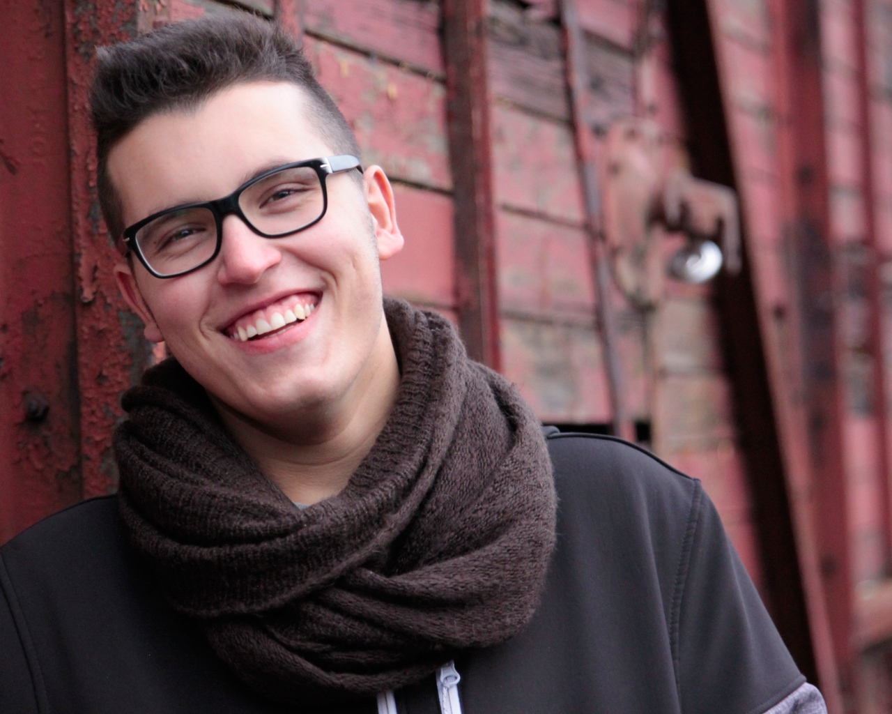 Улыбающийся мужчина в очках у стены 