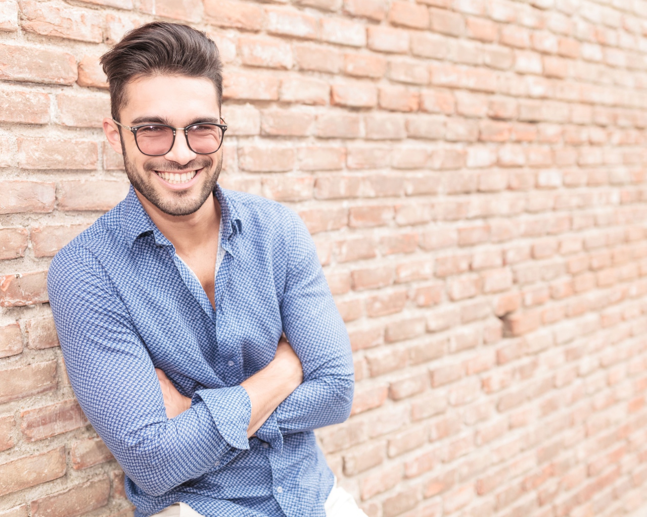Улыбающийся мужчина в очках стоит у стены 