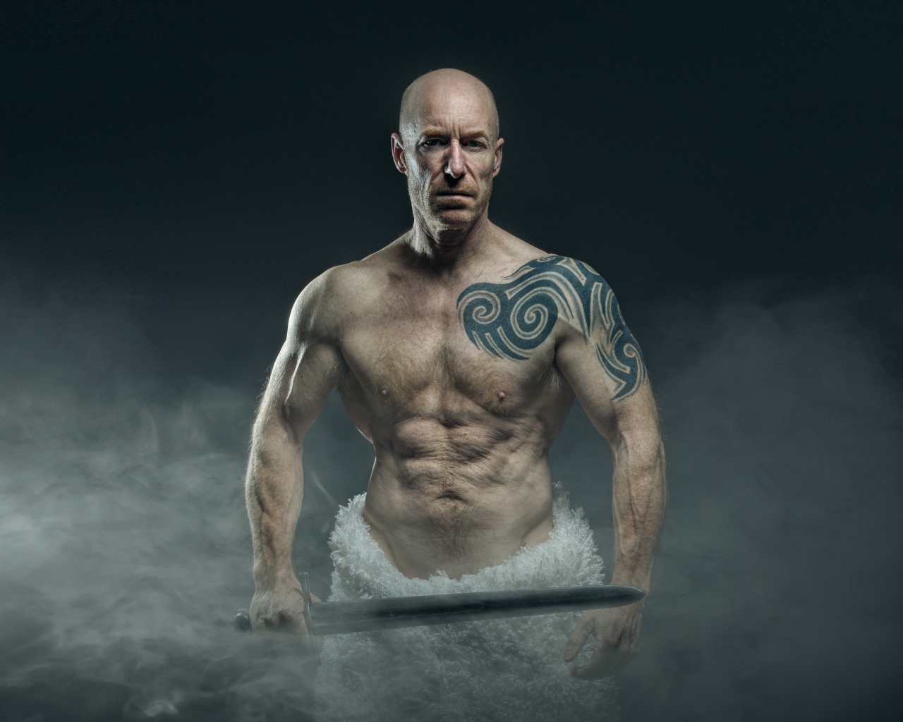 Сильный мужчина с мечом с татуировками на теле 