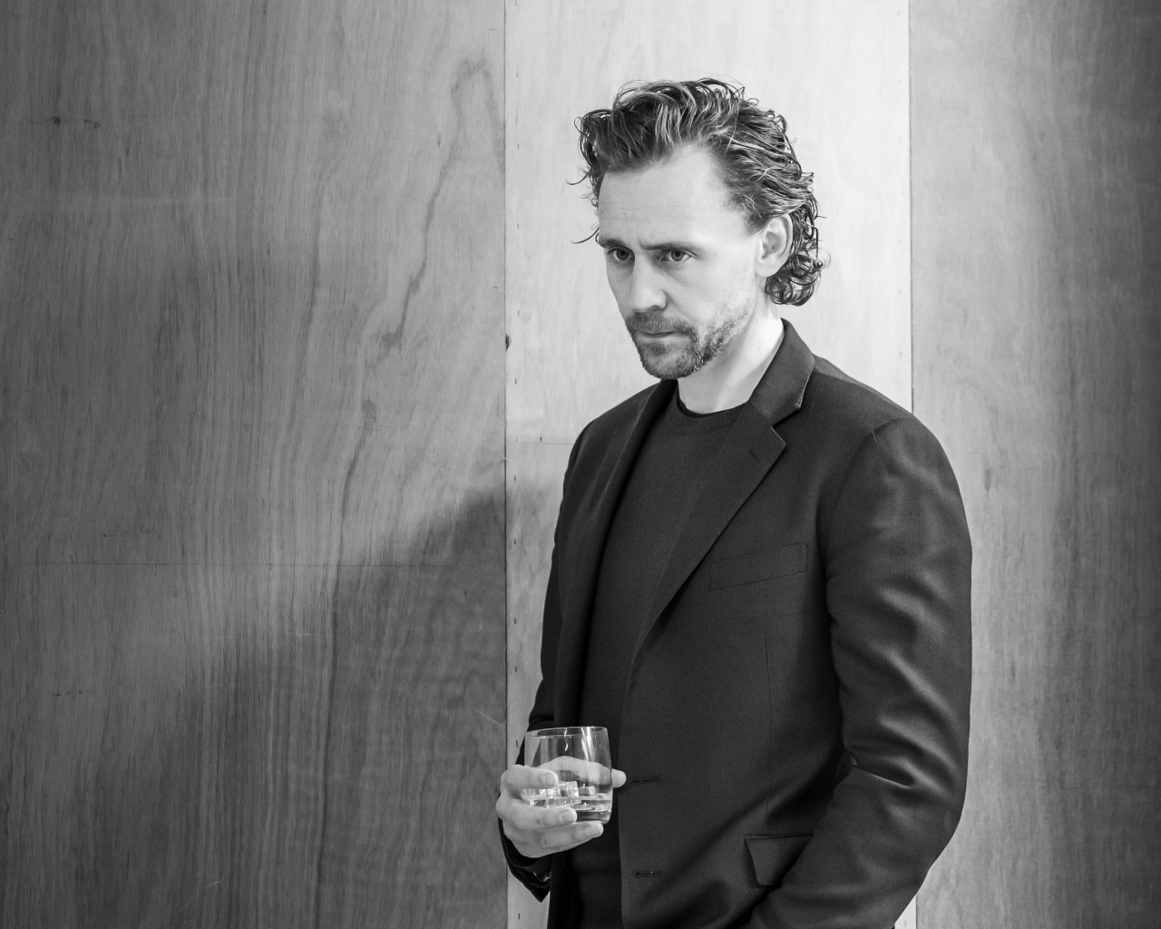 Актер Том Хиддлстон с бокалом в руке на фоне стены