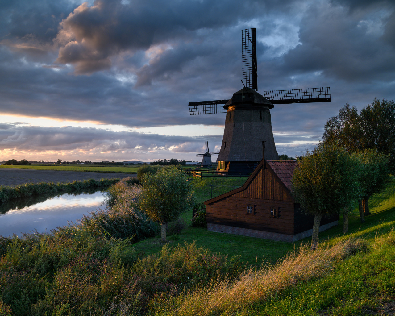 Большая ветряная мельница у реки на закате