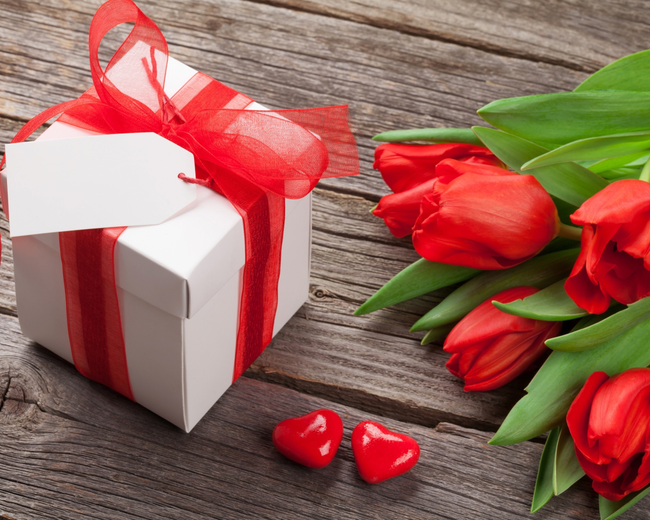 Красные тюльпаны с большим подарком на деревянном столе 