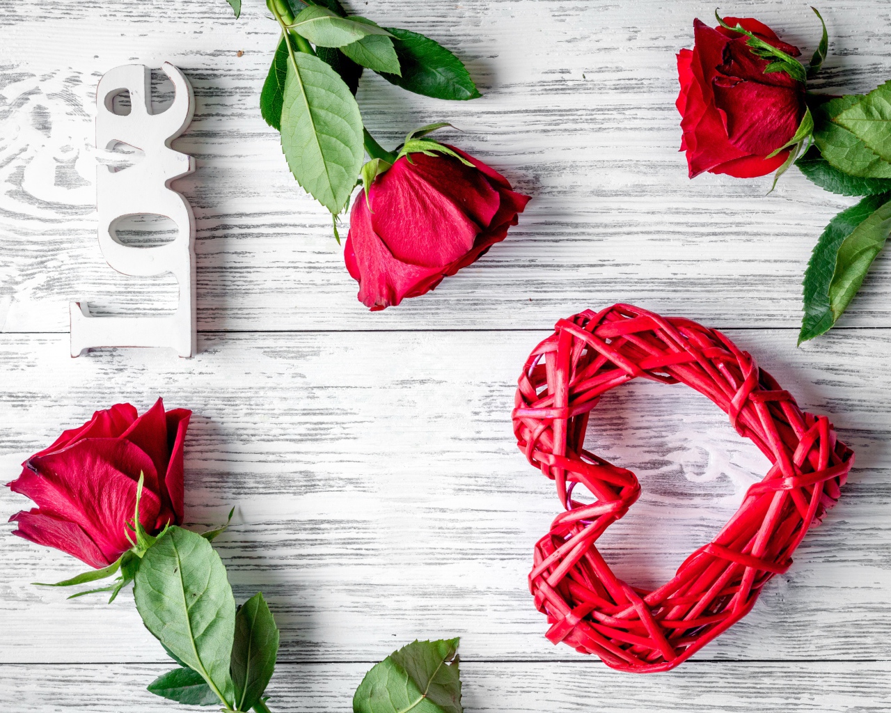 Красное плетеное сердце с алыми розами на деревянном столе