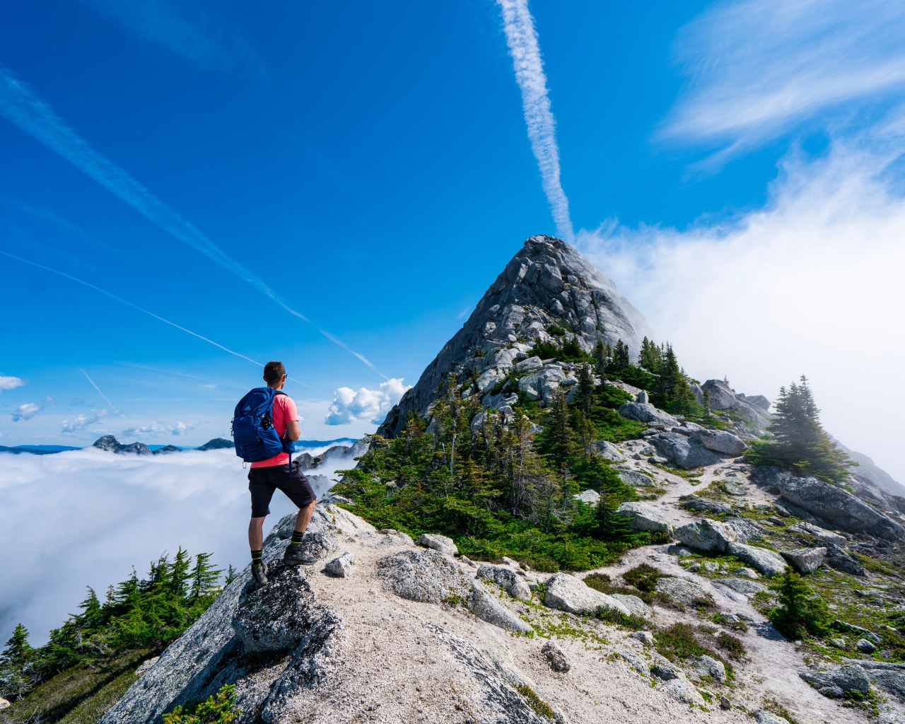 Мужчина подымается на вершина горы под голубым небом 